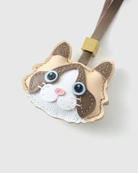 Tight close-up of the Cream Ragdoll face, angled — blue eyes in real leather, deep brown markings, pink nose. Every panel by hand.