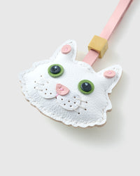 Tight close-up of the white Maine Coon face — large green eyes in real leather, pink inner ears, pink heart-shaped nose, layered fluff around the cheeks. Every panel by hand.