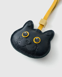 Tight close-up of the Black British Shorthair face — gold eyes in real leather, the round breed face, small black nose. Every panel by hand.