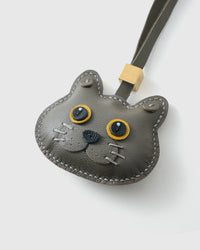 Tight close-up of the Blue British Shorthair face — gold eyes in real leather, the round breed face, small dark nose. Every panel by hand.