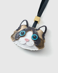 Tight close-up of the Ragdoll face — vivid blue eyes in real leather, bicolour caramel-and-brown markings, pink nose, white inner ears. Every panel by hand.