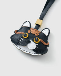 Both editions of the black long-hair tabby side by side — leather strap loop for bags, or 18K gold-plated keychain clip with engraved STICKYZOO disc.