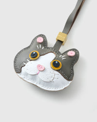 Tight close-up of the Grey Muse British Shorthair face — gold eyes in real leather, white face mask, pink inner ears, pink nose. Every panel by hand.