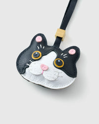 Tight close-up of the Black Muse British Shorthair face, angled — gold-orange eyes in real leather, white face mask, pink inner ears, pink nose. Every panel by hand.