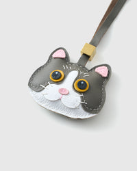 Tight close-up of the Grey Mist British Shorthair face — gold eyes in real leather, white face mask, pink nose, fine stitched whiskers. Every panel by hand.