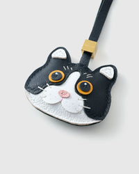 Tight close-up of the Black Mist British Shorthair face — gold-orange eyes in real leather, white face mask, pink nose, fine stitched whiskers. Every panel by hand.