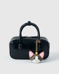 Taupe Devon Rex styled on a glossy black box bag, front — a small, specific piece that turns a simple bag into a personal one.