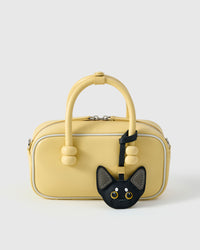 All-black Devon Rex with grey ears styled on a soft-yellow box bag, front — a small, specific piece that turns a simple bag into a personal one.