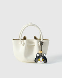 Black Ragdoll charm styled on an ivory bucket bag, front — a small, specific piece that turns a simple bag into a personal one.