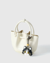 Black Ragdoll charm on an ivory bucket bag, side angle — real French leather, 3 days by hand.