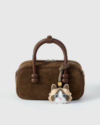 Cream Ragdoll styled on a dark brown suede top-handle bag, front — a small, specific piece that turns a simple bag into a personal one.