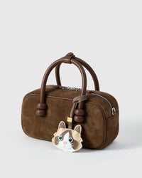 Cream Ragdoll charm on a dark brown suede top-handle bag, side angle — rated 4.9★ by thousands of buyers. Real French Alran leather, 3 days by hand.