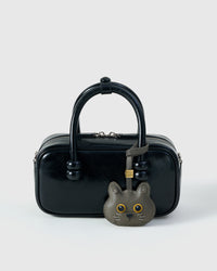Blue British Shorthair styled on a glossy black box bag, front — a small, specific piece that turns a simple bag into a personal one.