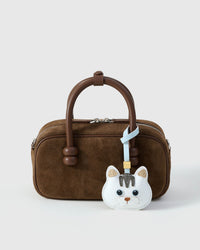 The Cloud Dream British Shorthair styled on a brown suede top-handle bag, front — a small, specific piece that turns a simple bag into a personal one.