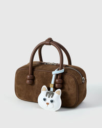 White British Shorthair charm on a brown suede bag, side angle — real French Alran leather, hand-cut over 3 days.