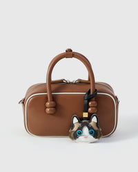 Ragdoll styled on a warm brown leather top-handle bag, front — a small, specific piece that turns a simple bag into a personal one.