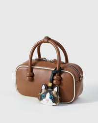 Ragdoll on a warm brown leather top-handle bag, side angle — Real French leather, 3 days by hand.