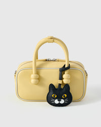 Chubby Midnight British Shorthair styled on a soft-yellow box bag, front — a small, specific piece that turns a simple bag into a personal one.