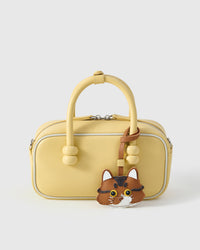 Orange long-hair tabby styled on a soft-yellow box bag, front — a small, specific piece that turns a simple bag into a personal one.