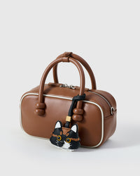 Black long-hair tabby on a tan leather top-handle bag, side angle — Real French leather, 3 days by hand.