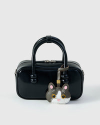Grey Muse British Shorthair styled on a glossy black box bag, front — a small, specific piece that turns a simple bag into a personal one.