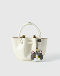 Grey Mist British Shorthair styled on a cream/ivory bucket bag, front — a small, specific piece that turns a simple bag into a personal one.
