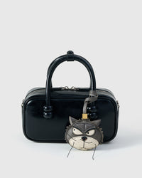 Grump cat charm styled on a glossy black box bag, front — real French leather, made to be carried on the bag that sees every day.
