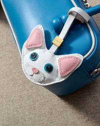 Snow-white Devon Rex cat charm hanging on a tan suede bag, side angle — real French leather, 3 days by hand.