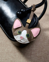 Taupe Devon Rex cat charm hanging on a glossy black box bag, close angle — real French Alran goatskin, 3 days by hand.