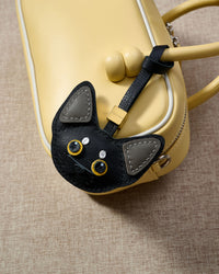 All-black Devon Rex with grey ears hanging on a bag, close angle — real French leather, 3 days by hand.