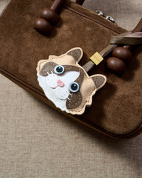 Cream Ragdoll charm close on a dark brown suede top-handle bag, side angle — real French Alran leather, 3 days by hand.