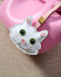 White Maine Coon charm close on a soft pink bucket bag, detail view — real French leather, 3 days by hand.