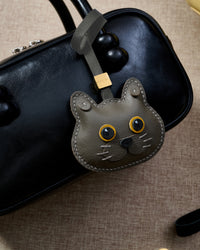 Blue British Shorthair close on a glossy black box bag, side angle — rated 4.9★ by thousands of buyers. Real French Alran leather, 3 days by hand.