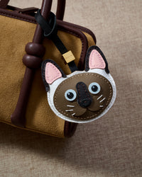 Close look at the Siamese face on a suede bag — layered cream-and-chocolate colour-point leather, blue eyes stitched in, pink ear interiors.