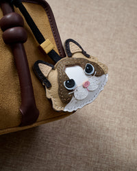 Ragdoll v.1 charm close on a tan suede top-handle bag, side angle — loved by thousands of cat people. Real French leather, 3 days by hand.
