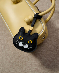 Chubby Midnight British Shorthair hanging on a soft-yellow box bag, close angle — real French leather, 3 days by hand.