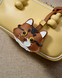 Orange long-hair tabby on a soft-yellow box bag, side angle — Real French leather, 3 days by hand.