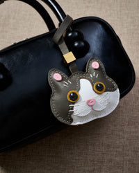 Grey Muse British Shorthair hanging on a glossy black box bag, close angle — 5,000+ reviews across STICKYZOO. Real French leather, 3 days by hand.