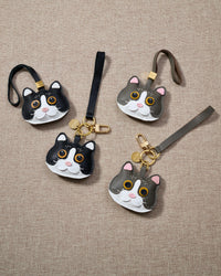 Overhead flatlay — Grey Mist British Shorthair charms with their black mist counterparts in strap and keychain editions. Finished one at a time, by hand.