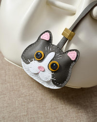 Grey Mist British Shorthair hanging on a cream/ivory bucket bag, close angle — loved by thousands of cat people. Real French leather, 3 days by hand.