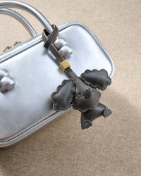 Close-up of handmade Poodle leather bag charm — hand-layered topknot curls in French Alran goatskin, hand-stitched edges. STICKYZOO Amsterdam design.