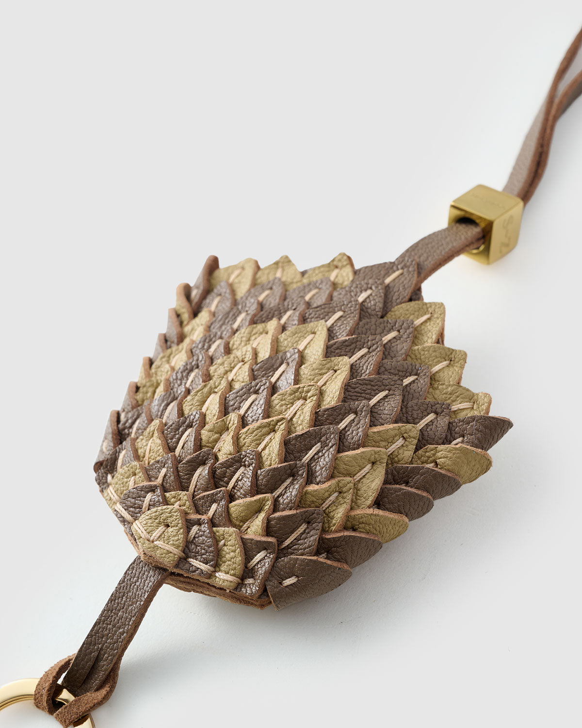 Close-up of the scaled charm — every scale cut and layered by hand in gold and taupe, stitched one by one.