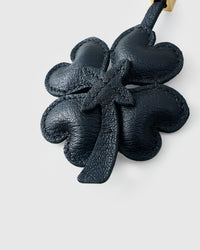 STICKYZOO Lucky Clover Charm clipped to a handbag — handmade French Alran goatskin in black padded 3D. 3-day artisan build.