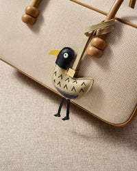 Gull charm styled on a bag, front — a small, specific piece that turns a simple bag into a personal one.