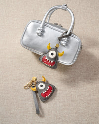 Close-up of the little monster — yellow horns, single white eye, hand-cut teeth in the red mouth. Every panel by hand.