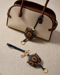 Both editions of the black-and-caramel scaled charm — leather strap for bags, or 18K gold-plated keychain clip.
