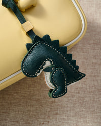 Both editions of the green dinosaur — leather strap loop for bags, or 18K gold-plated keychain clip.