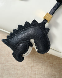 Both editions of the black dinosaur — leather strap loop for bags, or 18K gold-plated keychain clip.