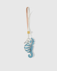 Blue seahorse charm handmade from French Alran genuine goatskin — soft sky-blue body, white chest, hand-stitched dorsal ridge, curled tail, cream-pink leather strap. Three days by hand. Arrives in luxury gift packaging. Designed in Amsterdam.