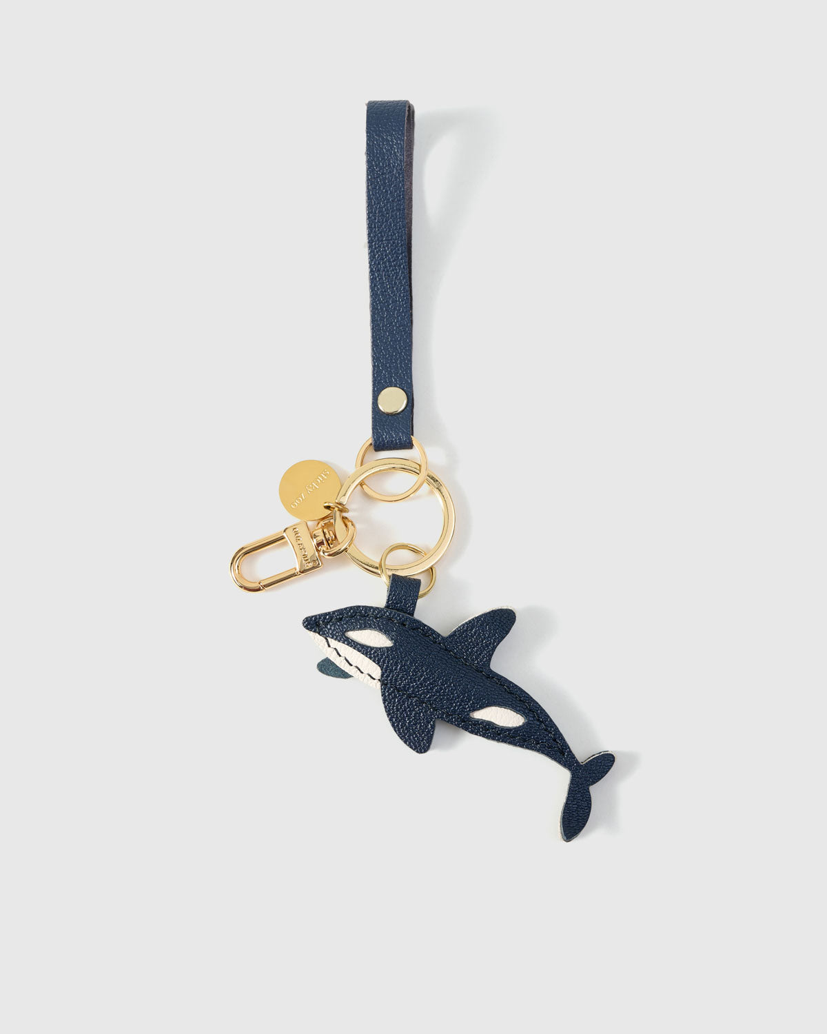 {{Dual attachment.}} Both editions of the orca — leather strap loop for bags, or 18K gold-plated keychain clip.